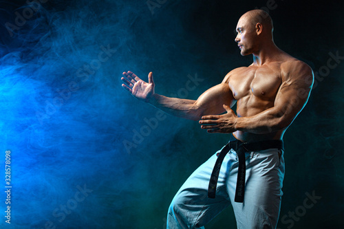 Karate or taekwondo fighter on black background with smoke. Fit man sportsmen bodybuilder physique and athlete. Men's sport motivation.