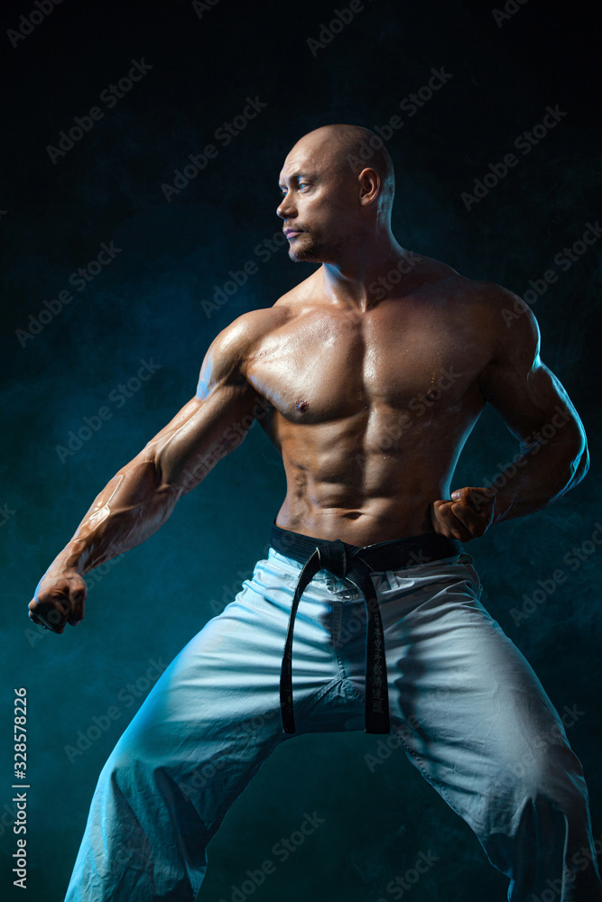 Karate or taekwondo fighter on black background with smoke. Fit man