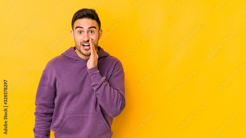 Young caucasian man isolated on yellow bakground is saying a secret hot braking news and looking aside