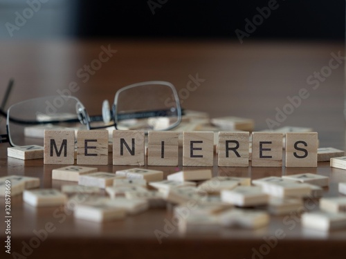 menieres concept represented by wooden letter tiles on a wooden table with glasses and a book photo