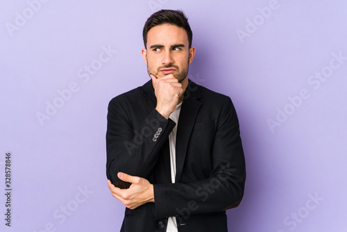 Young caucasian man isolated on purple background looking sideways with doubtful and skeptical expression.