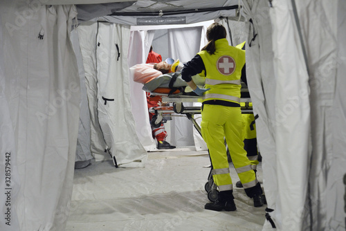 Doctor with protection mask checking patient with Corona Virus on the stretcher inside a hospital field tent for the first AID. Camp room for people infected with an epidemic. photo