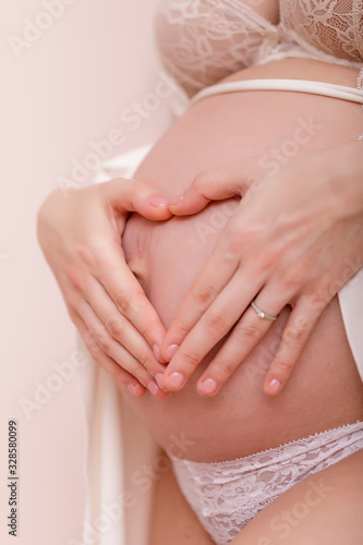 Closeup of pregnant woman holding her hands on her swollen belly shaping a heart, toned in pastel colors.