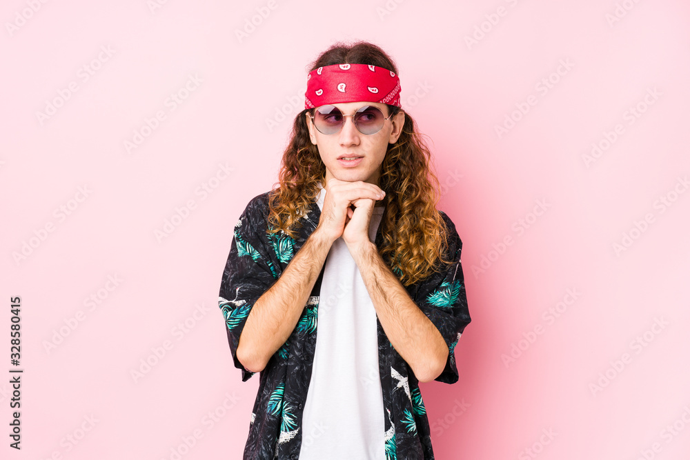Young hippie caucasian man isolated keeps hands under chin, is looking happily aside.