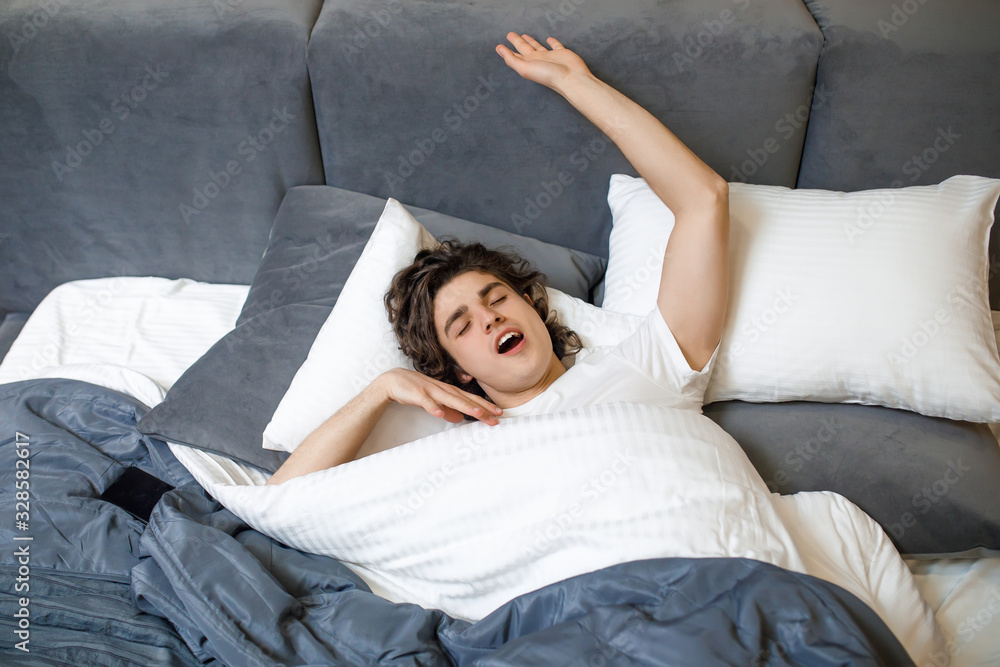 Image of a handsome young man in the morning yawning and stretching in modern bed Image of a handsome young man in the morning yawning and stretching in modern bed