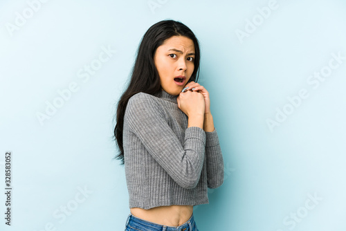 Young chinese woman isolated on a blue background scared and afraid. © Asier