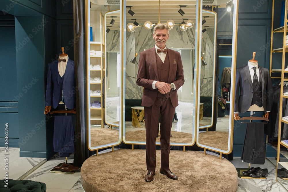 Cute mature millionaire in glasses on the fitting of a new exclusive suit in an elite boutique.