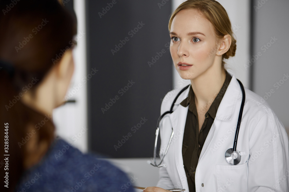 Cheerful smiling female doctor and patient woman discussing current health examination while sitting in clinic. Perfect medical service in hospital. Medicine concept Cheerful smiling female doctor and patient woman discussing current health examination while sitting in clinic. Perfect medical service in hospital. Medicine concept