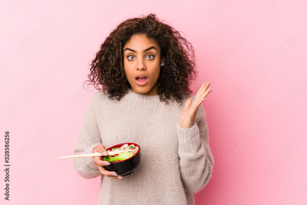 Young african american woman eating noodles surprised and shocked. Young african american woman eating noodles surprised and shocked.