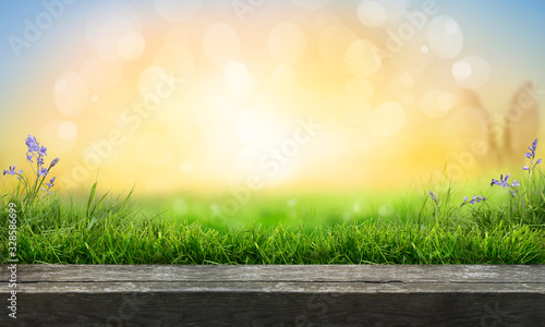 A wooden table top product display with a fresh sunny Easter background of blue sky and  warm bokeh with green grass meadow foreground.