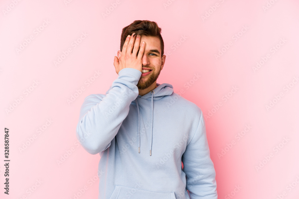 Young caucasian man isolated on pink background having fun covering half of face with palm. Young caucasian man isolated on pink background having fun covering half of face with palm.