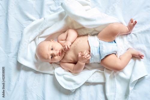 Little baby in diaper lying on bed at home looking aside concerned top view