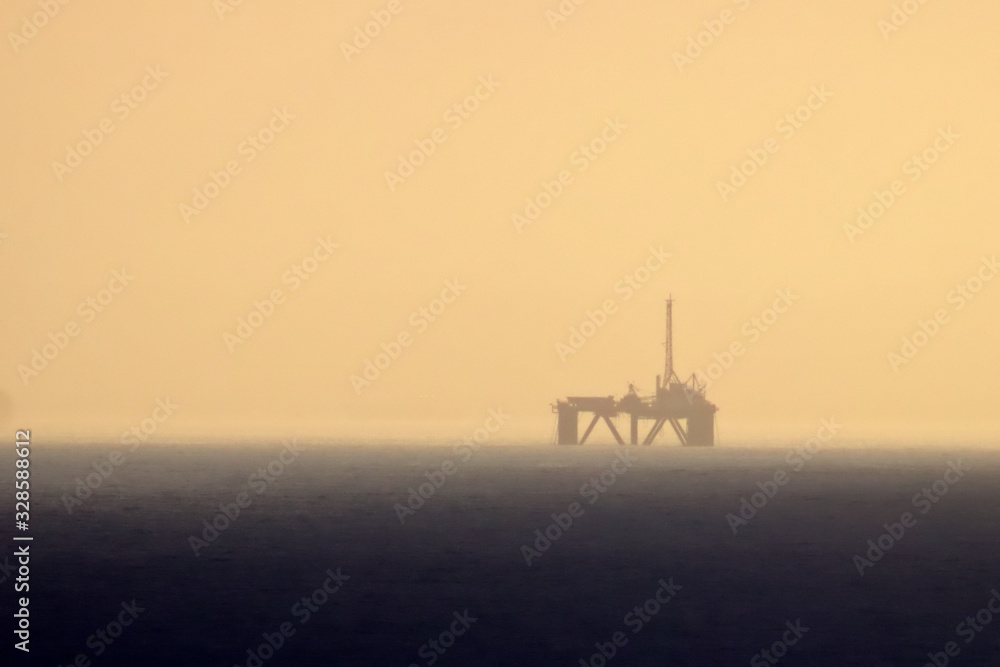 The gas rig out at sea through a hazy sky as the sun sets over the ocean in Mosselbay, South Africa