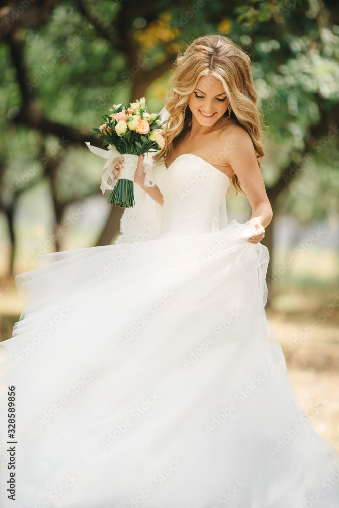 Cute young bride with long hairs holding her wedding bouquet includes white roses and other flowers. Beautiful white marriage dress. Pretty girl on greet trees background Cute young bride with long hairs holding her wedding bouquet includes white roses and other flowers. Beautiful white marriage dress. Pretty girl on greet trees background
