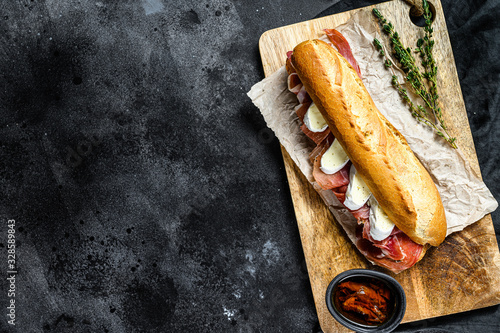 baguette sandwich with jamon ham serrano, paleta iberica, Camembert cheese on the cutting Board.  Black background, top view, space for text photo