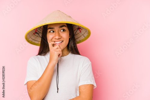 Young asian woman wearing a vietnamese hat isolated Young asian woman wearing a vietnamin hatrelaxed thinking about something looking at a copy space.