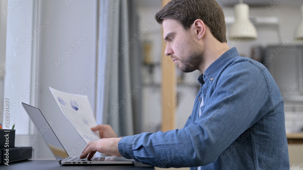 Young Man Entering Data from Documents to Laptop Young Man Entering Data from Documents to Laptop
