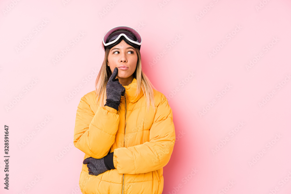 Young caucasian woman wearing a ski clothes in a pink background looking sideways with doubtful and skeptical expression.