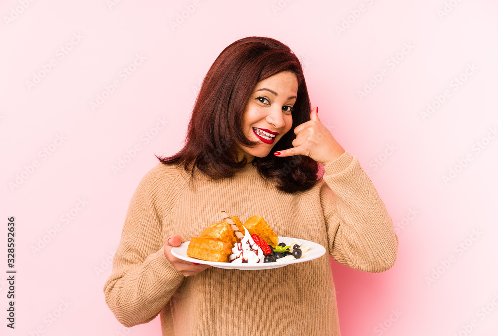 Middle age latin woman holding a waffle isolated showing a mobile phone call gesture with fingers.