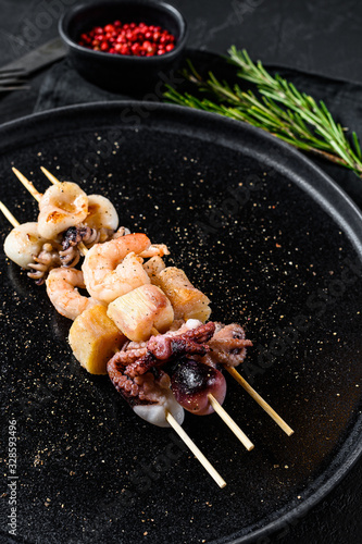 Barbecue with seafood. Kebab on wooden skewers with shrimp, octopus, squid and mussels. Black background. Top view