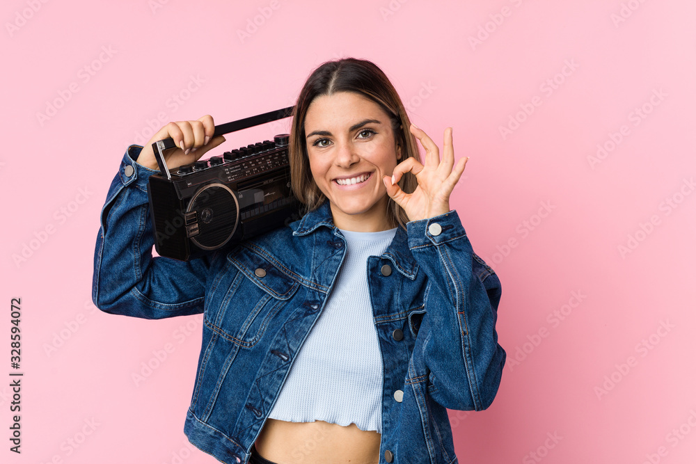 Young caucasian woman holding a guetto blaster cheerful and confident showing ok gesture. Young caucasian woman holding a guetto blaster cheerful and confident showing ok gesture.