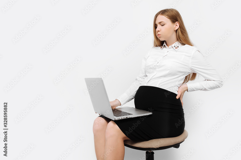 Image of a young pregnant businesswoman in glasses, tired girl working with laptop, sitting on a chair Image of a young pregnant businesswoman in glasses, tired girl working with laptop, sitting on a chair