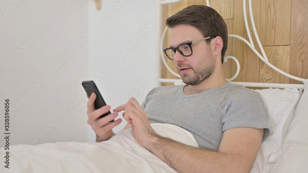 Young Man using Smartphone in Bed Young Man using Smartphone in Bed