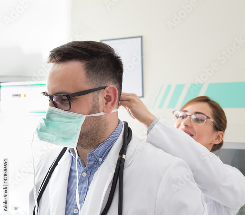 Nurse tying protective mask to doctor