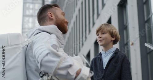 Wallpaper Mural Rear of handsome man spaceman in space suit talking with cute small schoolboy outdoors and telling about cosmos. Male astronaut with little boy standing at street and having nice conversation. Torontodigital.ca