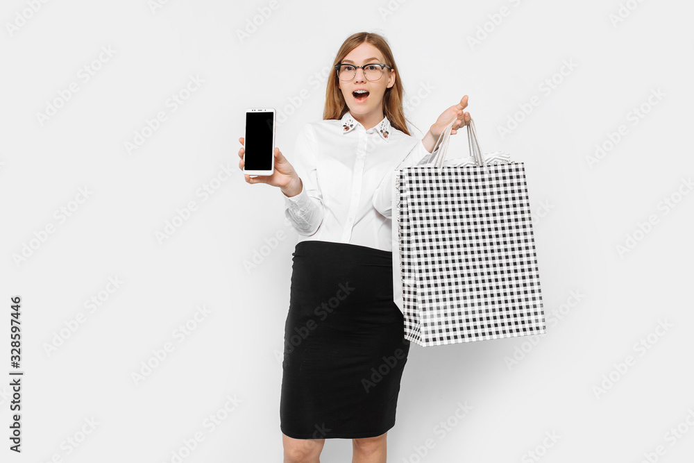 Image of a young pregnant businesswoman wearing glasses, shows a blank smartphone screen, with packages in hand, shopping Image of a young pregnant businesswoman wearing glasses, shows a blank smartphone screen, with packages in hand, shopping
