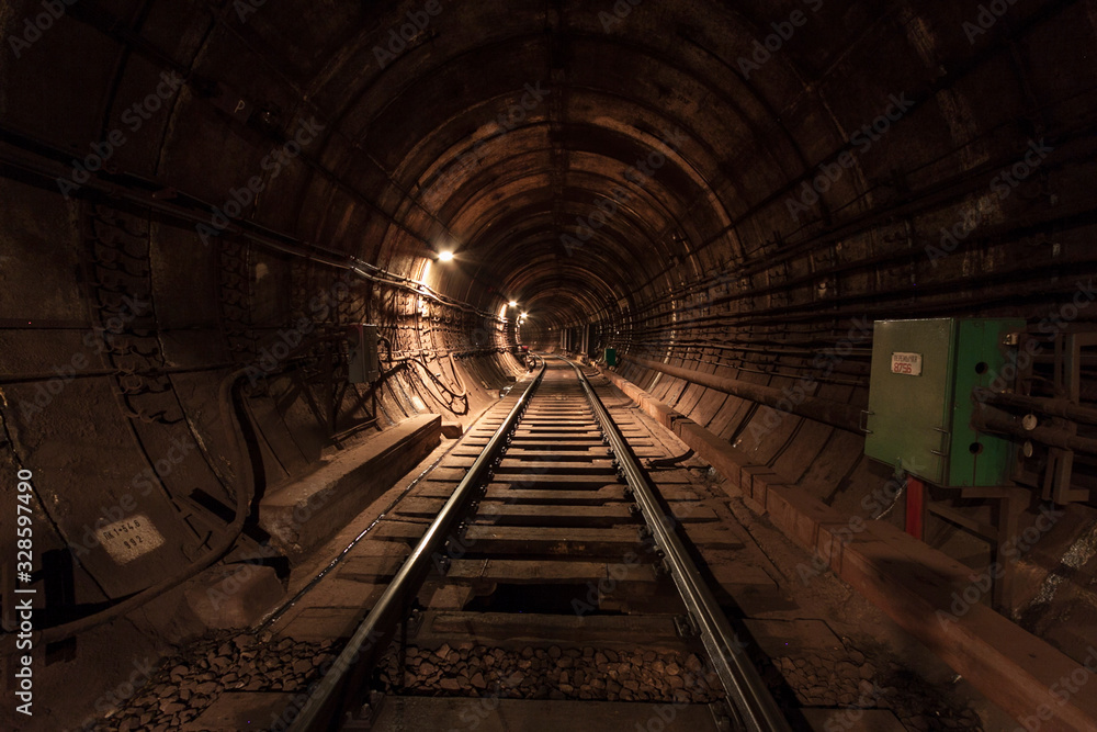 A lighted reinforced concrete subway tunnel, cable routes are laid, the railroad tracks turn left. In front of them are iron vertical boxes of automatics.