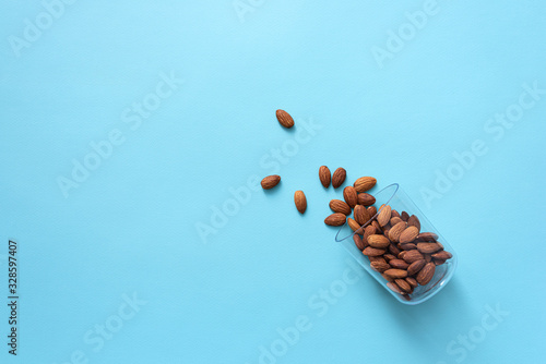 A glass lies on its side with almond nuts poured out of it. Top view healthy food background.