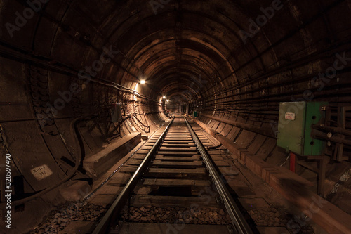 A lighted reinforced concrete subway tunnel, cable routes are laid, the railroad tracks turn left. In front of them are iron vertical boxes of automatics.