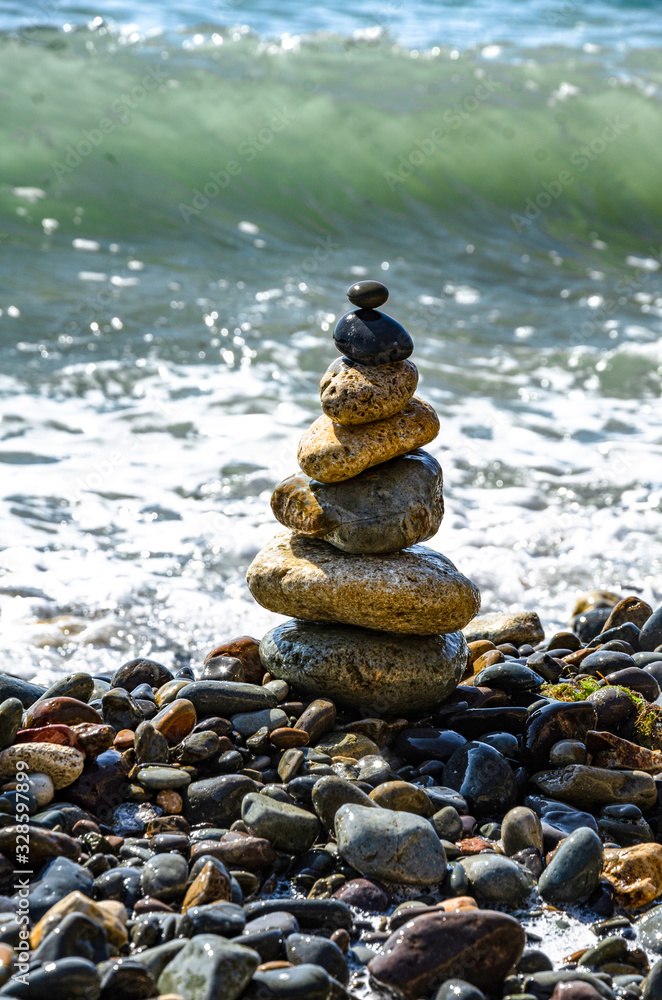 A pebble pyramid on a background of a sea wave. Rest and travel.