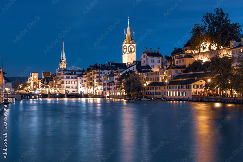 Famous Fraumunster and Church of St Peter with reflections in river Limmat at night in Old Town of Zurich, the largest city in Switzerland