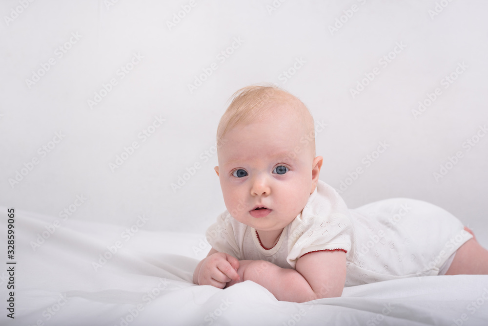 Funny little baby lying down on white blanket. Textile and bedding for kids.