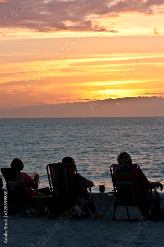 Back view, medium distance of senior couples, siting on beach chairs, watching a sunset on the shore of a tropical sandy beach, on gulf of mexico