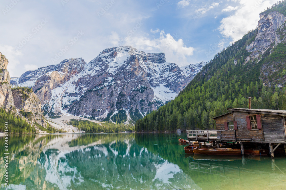 landscape of Lago di Braies, impressive green lake, which reflects the high snowy mountains, surrounded by abundant green vegetation, we can also see a wooden cabin that is the jetty and some wooden b