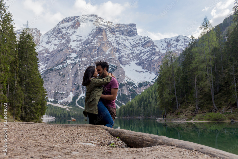 Loving couple on Lago di Braies, impressive green lake, which reflects the high snowy mountains, surrounded by abundant green vegetation