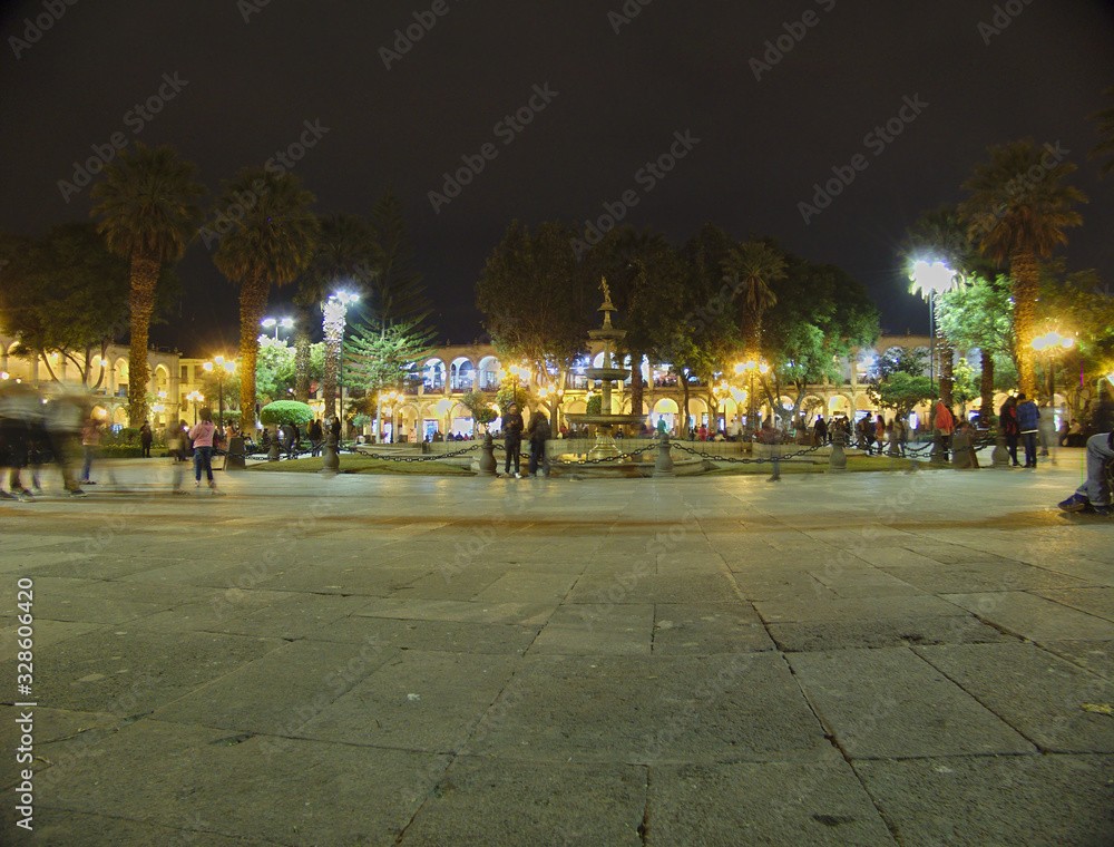 Arequipa's main square at night, illuminated with people walking in it.