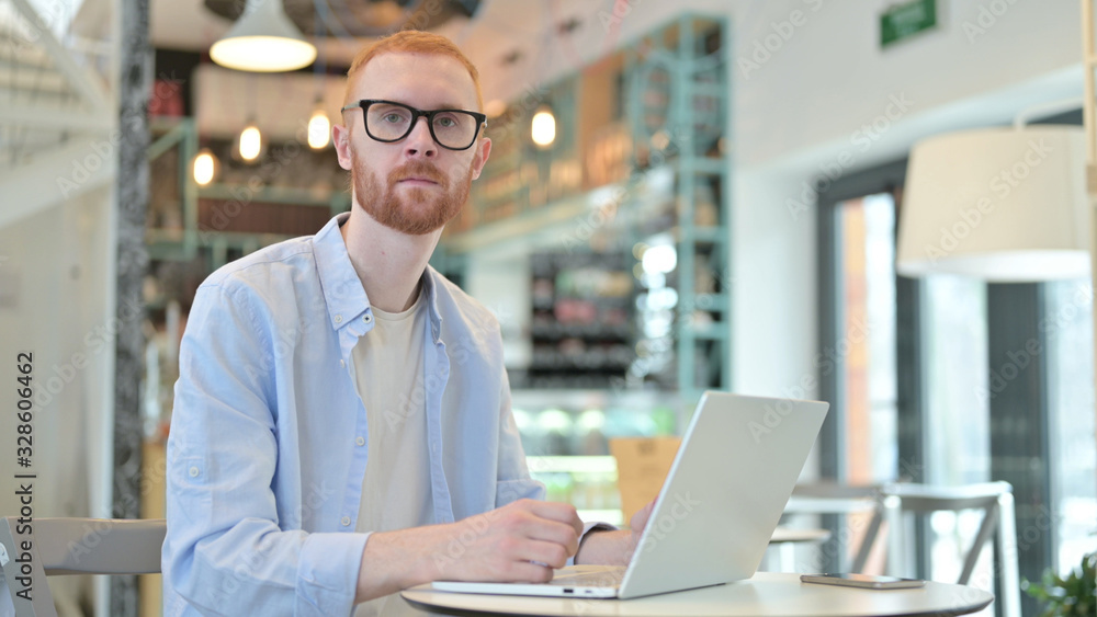 Redhead Man with Laptop Looking at Camera in Cafe Redhead Man with Laptop Looking at Camera in Cafe