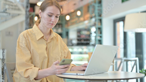 Young Woman using Smartphone and Laptop in Cafe