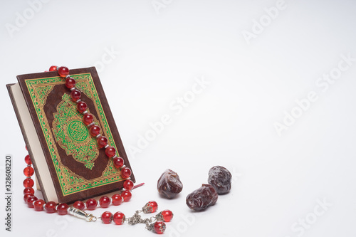 Faith in Islam concept. The Islamic holy book, Quran or Kuran, with rosary beads or “tasbih” and dates (kurma)  isolated on white background. photo