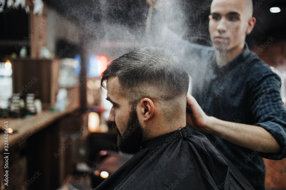 Good looking young adult man getting a hair and beard styling and dressing treatment by professional hairstylist. Good looking young adult man getting a hair and beard styling and dressing treatment by professional hairstylist.