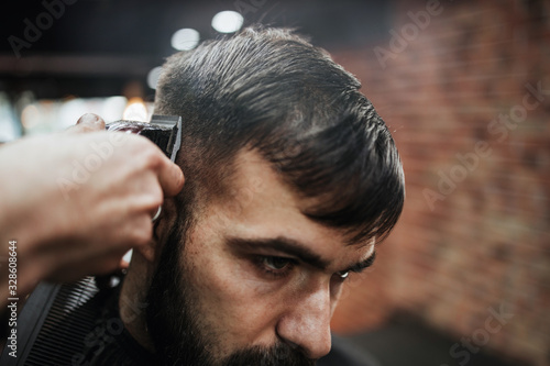 Good looking young adult man getting a hair and beard styling and dressing treatment by professional hairstylist.