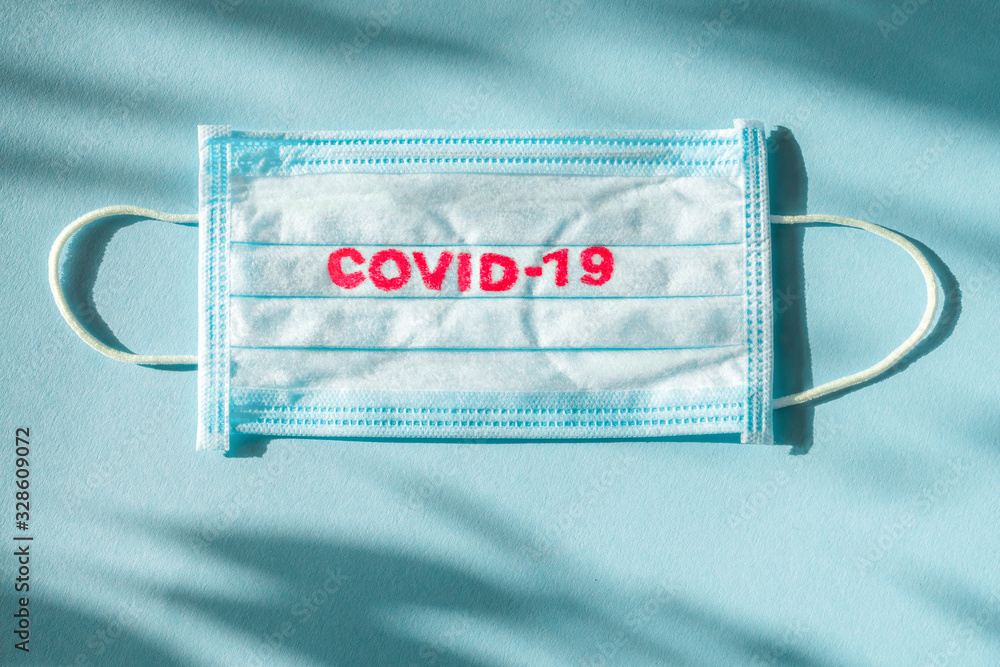 Covid-19 - Wuhan Novel Coronavirus pneumonia gets official name from WHO: COVID-19. Disposable dressing on the face. Healthcare background. Blue medical disposable face mask with covid-19 print Covid-19 - Wuhan Novel Coronavirus pneumonia gets official name from WHO: COVID-19. Disposable dressing on the face. Healthcare background. Blue medical disposable face mask with covid-19 print