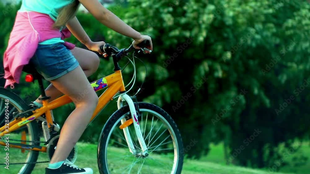 Child put on bicycle helmet teach ride bike in summer park . Girl is riding down hill on hight speed. Child put on bicycle helmet teach ride bike in summer park . Girl is riding down hill on hight speed.