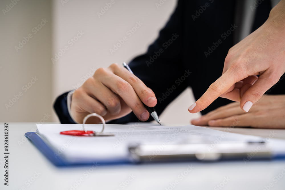 Person's Hand Signing Contract With Keys On It Person's Hand Signing Contract With Keys On It