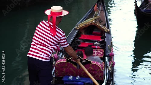 Gondolier navigating traditional gondola in Venice canal. Famous historic landmark in Italy. Summer tourism vacation & family travel destination in Europe. Slow motion. 