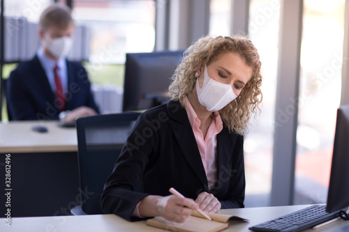 Business woman with curly blonde hair wearing a mask sitting in office, Concept,contagious disease, coronavirus, covid2019 photo